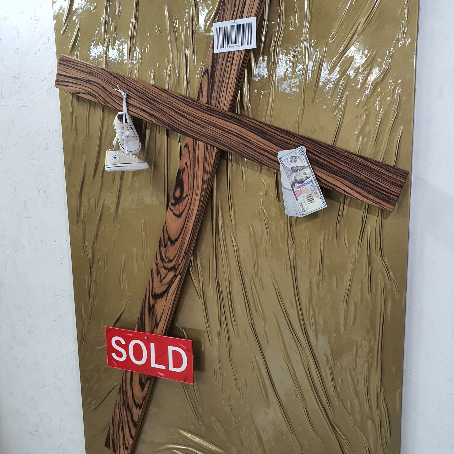 Il Settimo Comandamento mixed media artwork – close-up of cross pierced with baby shoes, dollar bills and red SOLD label