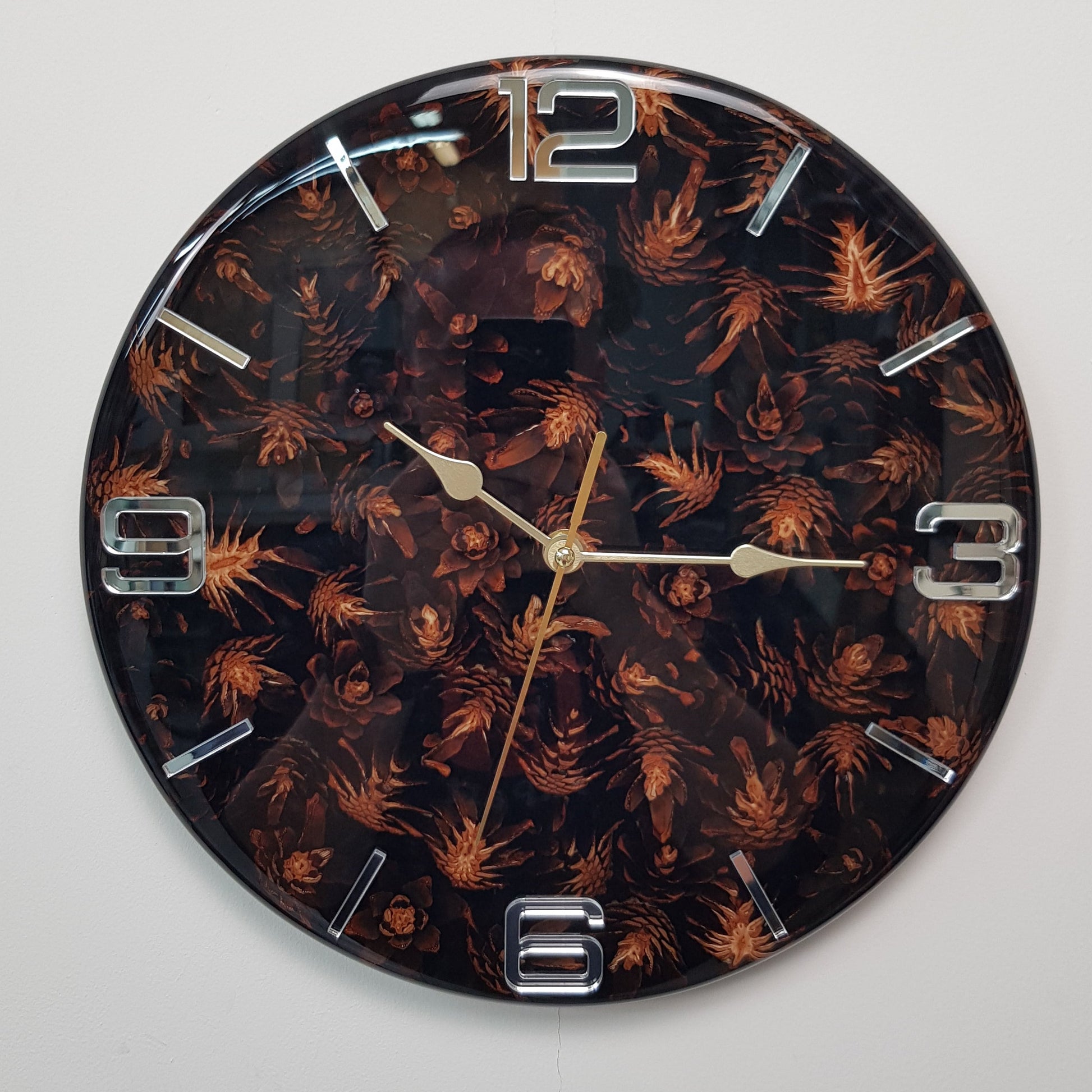 Front view of the “Pine Shadows” wall clock showing black resin, pine cones, and mirrored silver markers