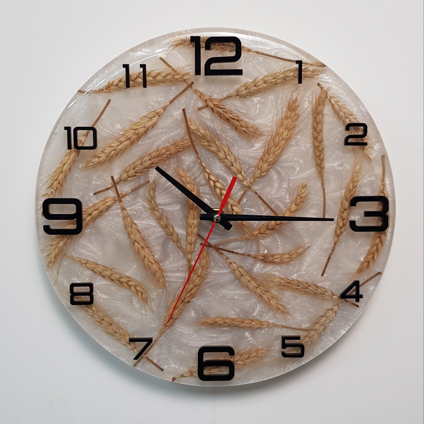 Front view of the “Fields of Time” clock showing wheat stalks embedded in pearlescent resin with black plexiglass numbers.