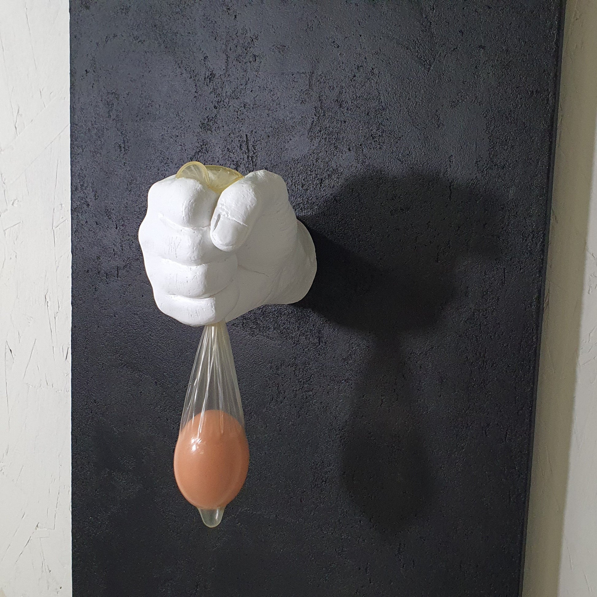 Vita Protetta resin and plaster conceptual artwork – close-up of symbolic hand gripping condom with egg
