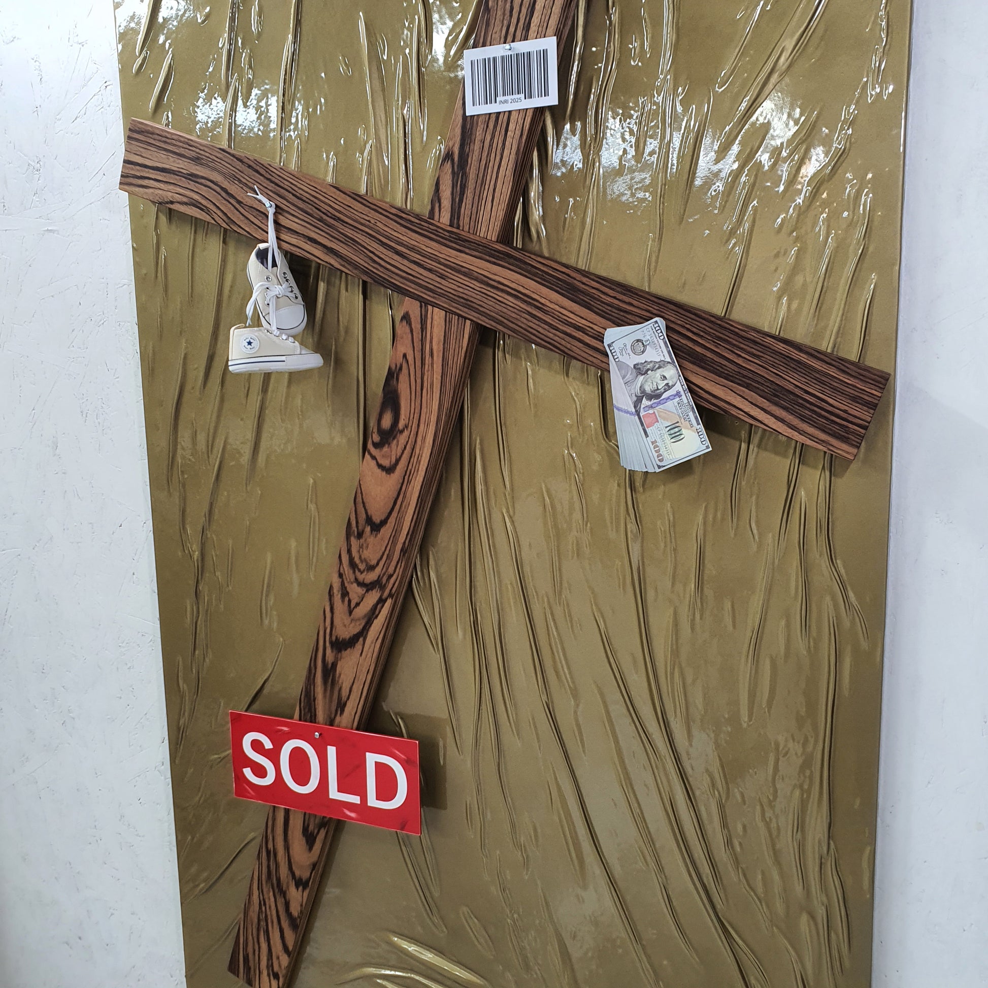 Il Settimo Comandamento mixed media artwork – close-up of cross pierced with baby shoes, dollar bills and red SOLD label