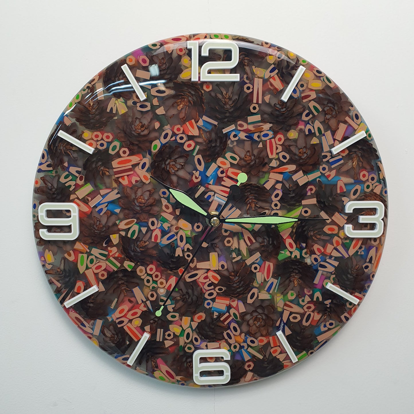 Front view of the “Pine & Color Fusion” wall clock made from colorful pencils and pinecones embedded in epoxy resin, with glowing white plexiglass numbers.