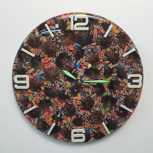 Front view of the “Pine & Color Fusion” wall clock made from colorful pencils and pinecones embedded in epoxy resin, with glowing white plexiglass numbers.