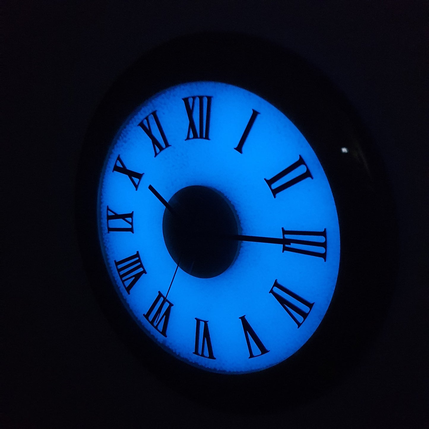 Side night view of glowing Roman numeral wall clock showing illuminated resin surface.