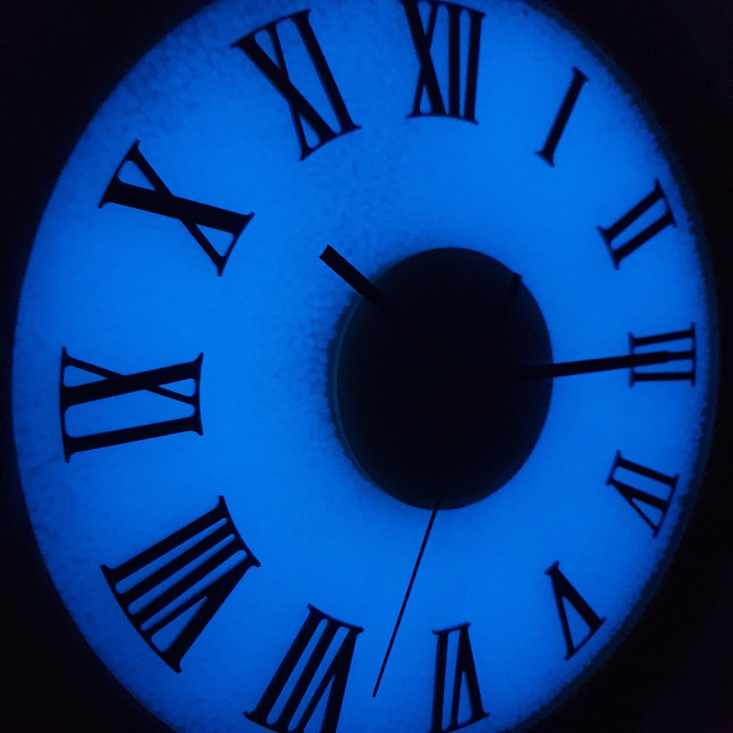Close-up night view of fluorescent Roman numeral clock glowing blue in the dark.