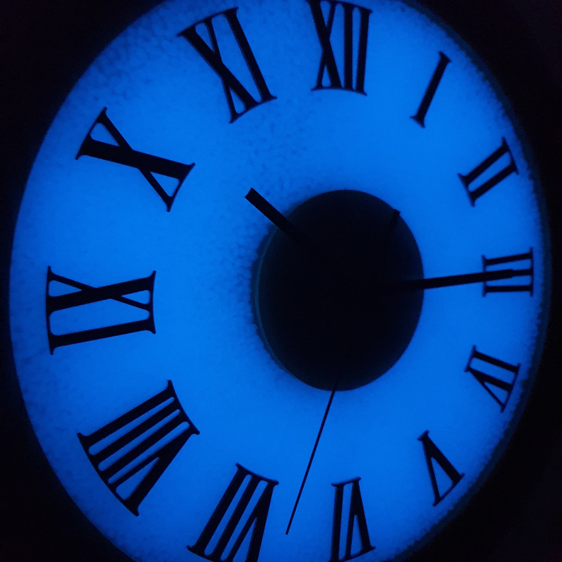 Close-up night view of fluorescent Roman numeral clock glowing blue in the dark.