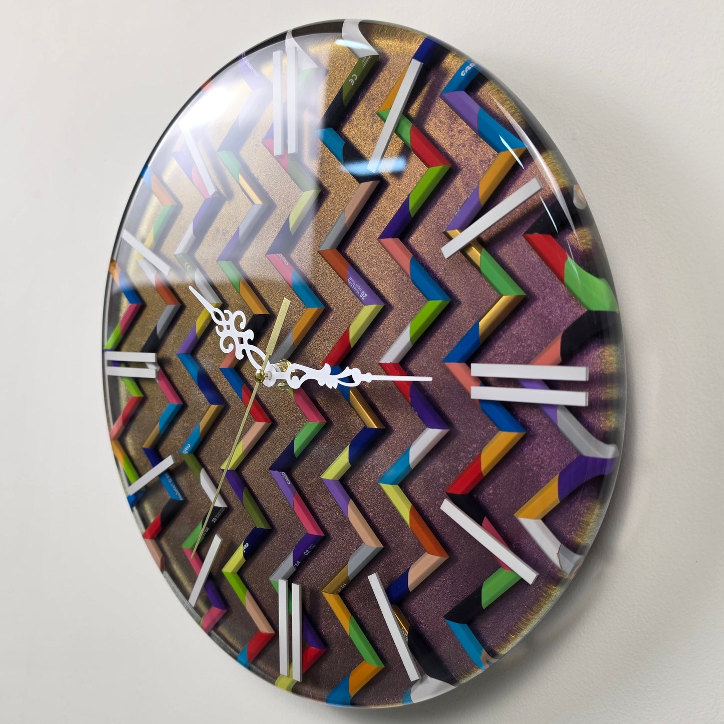 Studio Colors artistic wall clock made with real colored pencil pieces arranged in a repeating colorful chevron pattern.