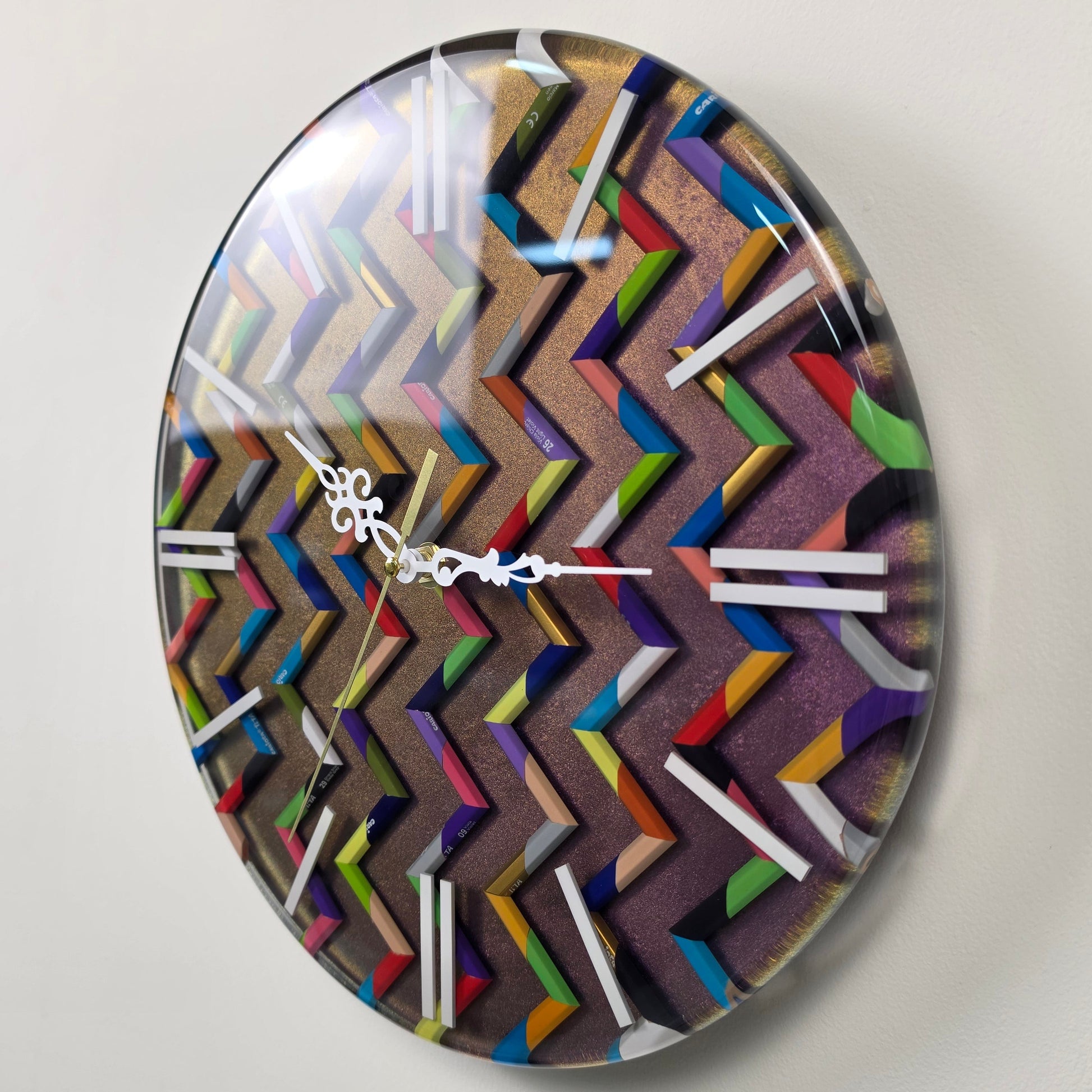 Studio Colors artistic wall clock made with real colored pencil pieces arranged in a repeating colorful chevron pattern.