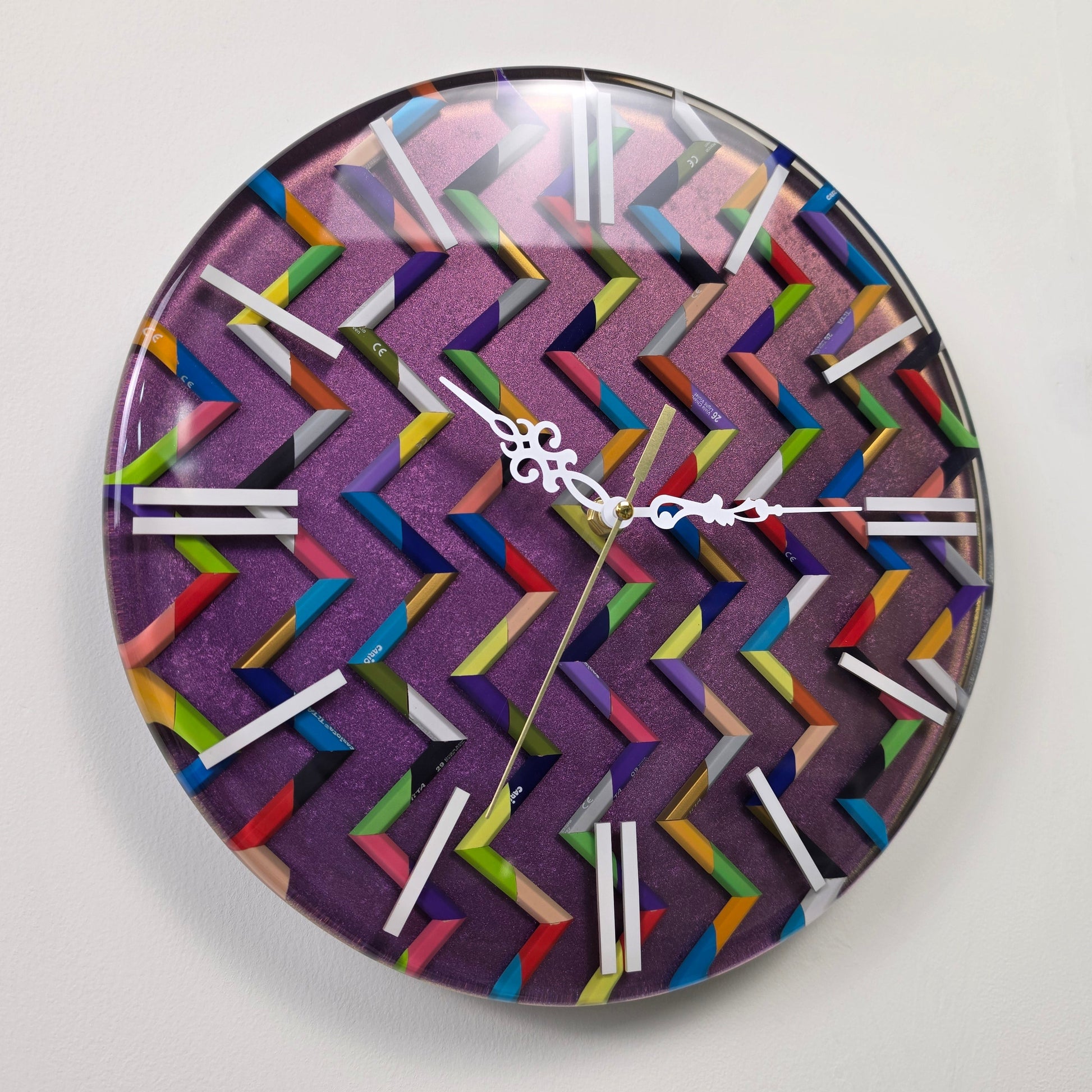 Handmade epoxy resin wall clock with multicolored pencil fragments, white hour markers and decorative white hands.