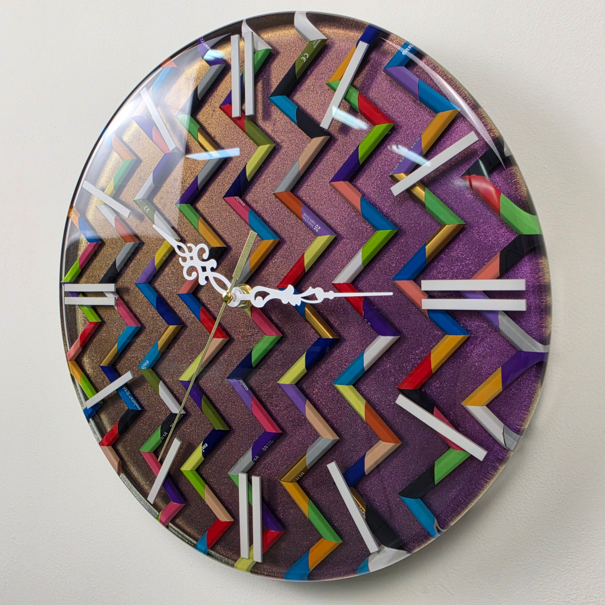 Modern geometric wall clock featuring colorful pencils, shimmering metallic background and glossy clear resin surface.