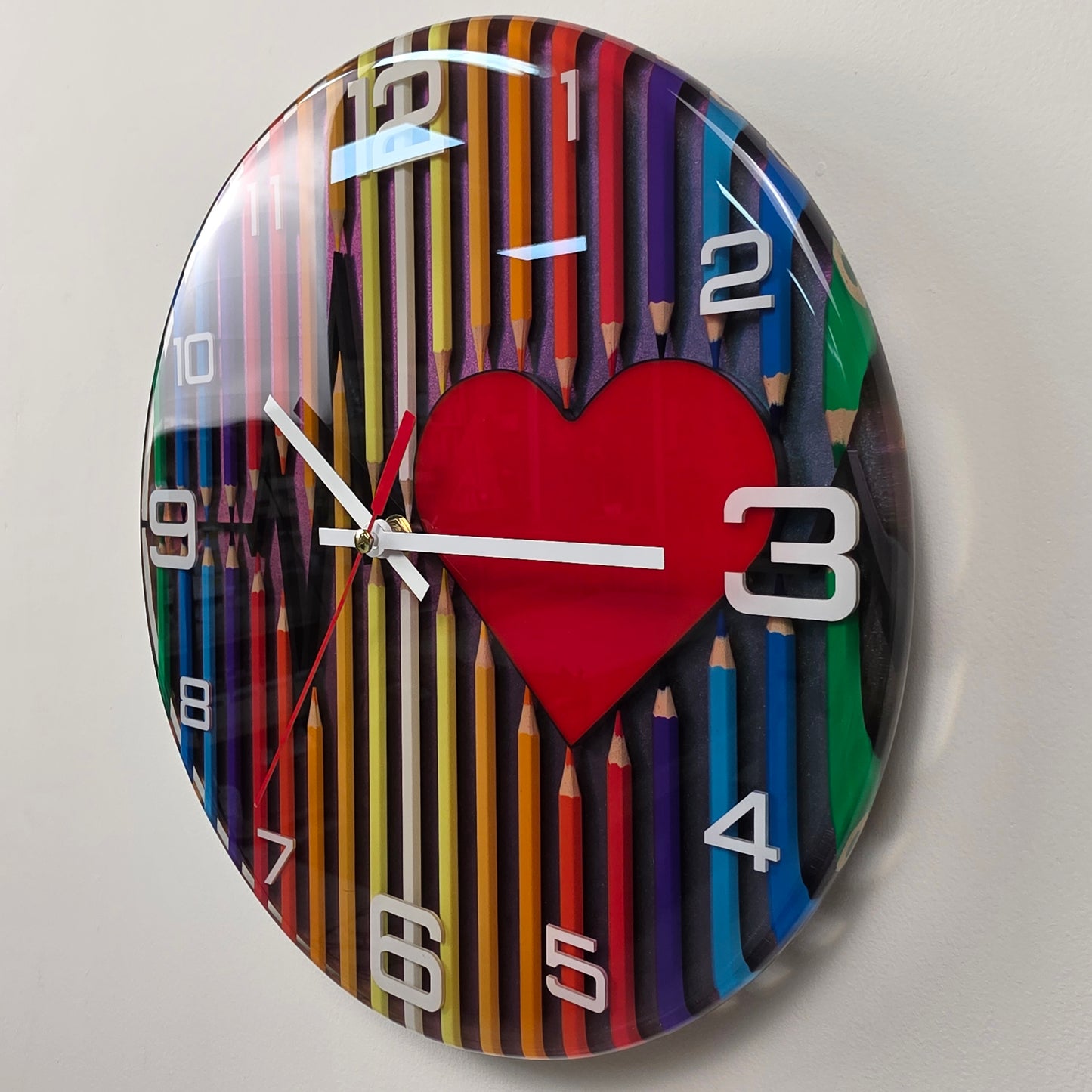 Unique 30 cm epoxy resin wall clock with colorful pencil composition, heart motif, silent quartz movement, and shimmering chameleon finish.