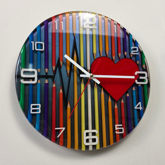 Handcrafted epoxy resin wall clock featuring colorful pencils, a heartbeat line, and a red heart on a chameleon background with white acrylic numbers from the Abstract Time collection.