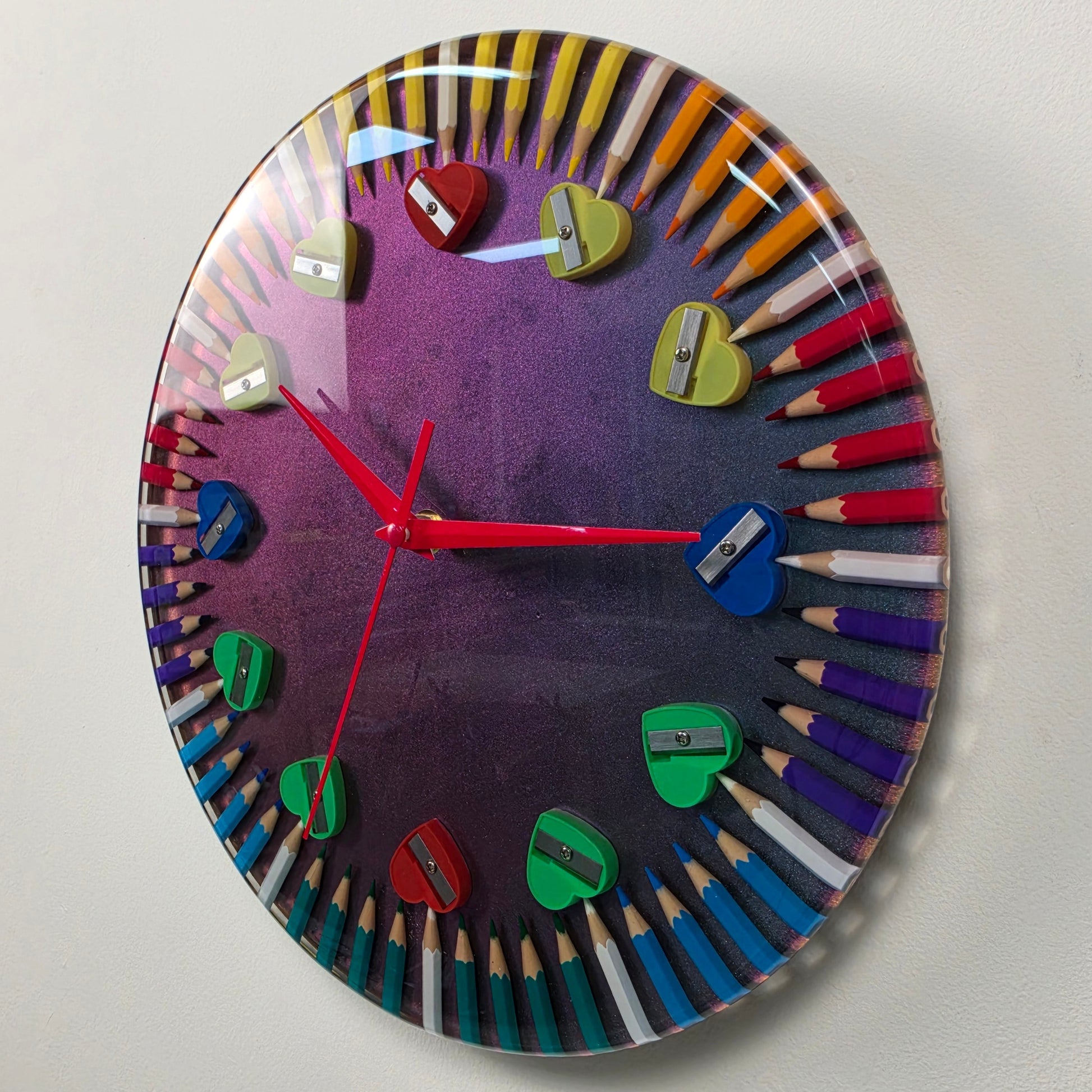 Modern artistic wall clock with colorful pencils arranged in a circle and decorative heart sharpeners.
