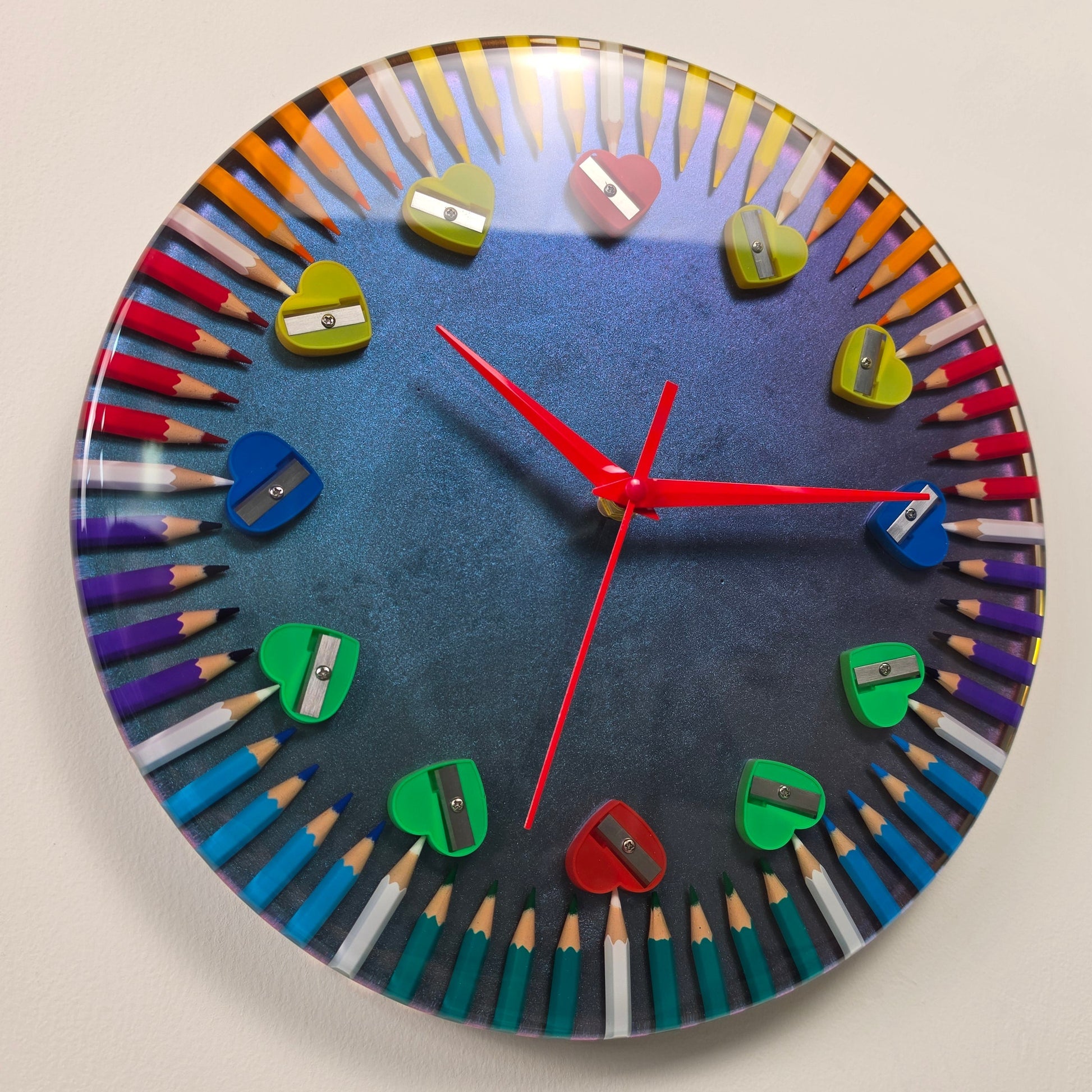 Handmade epoxy resin wall clock with colored pencils and heart-shaped pencil sharpeners on a chameleon background.