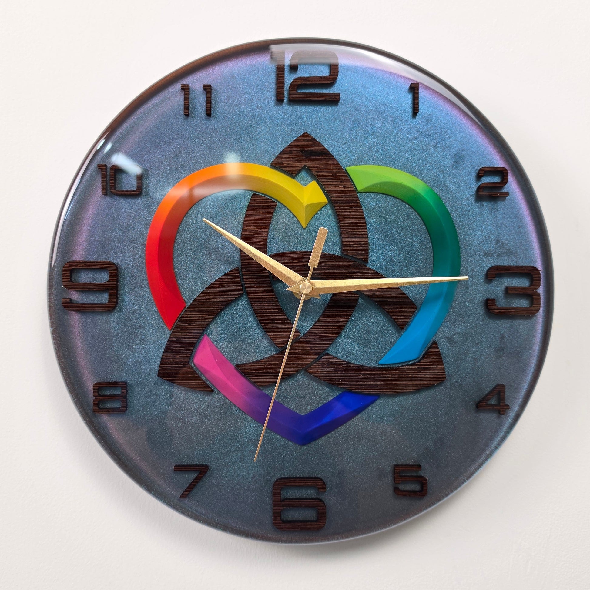 Unique 30 cm epoxy resin wall clock inspired by the ancient Triquetra symbol, combining handcrafted wenge wood with a shimmering chameleon finish.