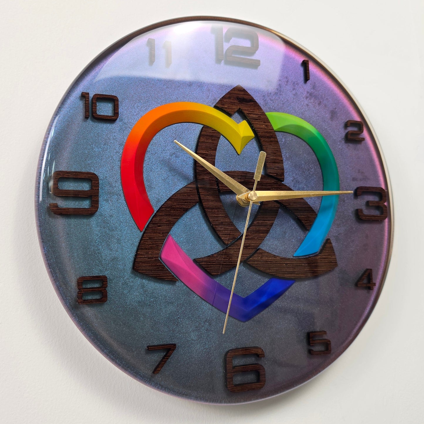 Handcrafted epoxy resin wall clock featuring a wenge wood Triquetra symbol, rainbow heart, and chameleon background from the Timeless Symbols collection.