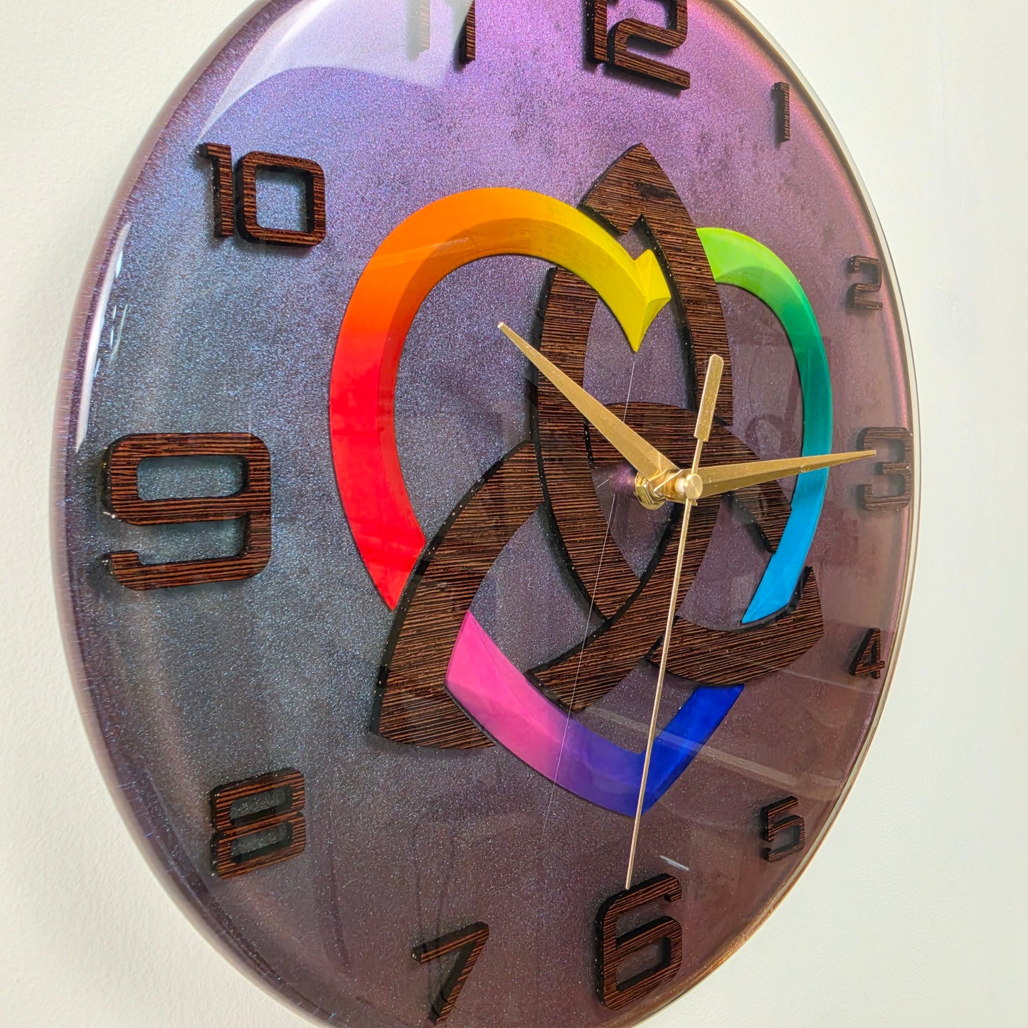 Modern resin wall clock with a handcrafted wenge wood Triquetra, rainbow-colored heart, wooden numbers, and silent quartz movement.