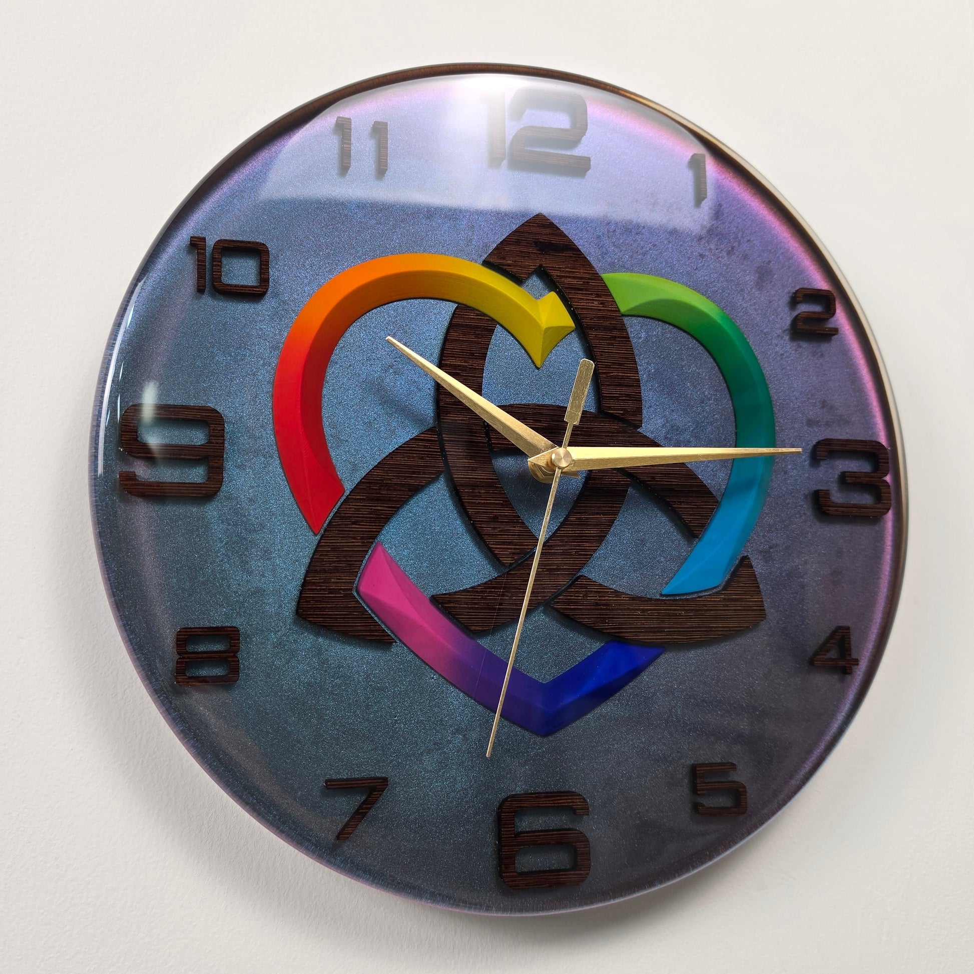 Artistic epoxy resin wall clock with a wenge wood Celtic knot, rainbow heart centerpiece, silent sweep movement, and iridescent chameleon effect.