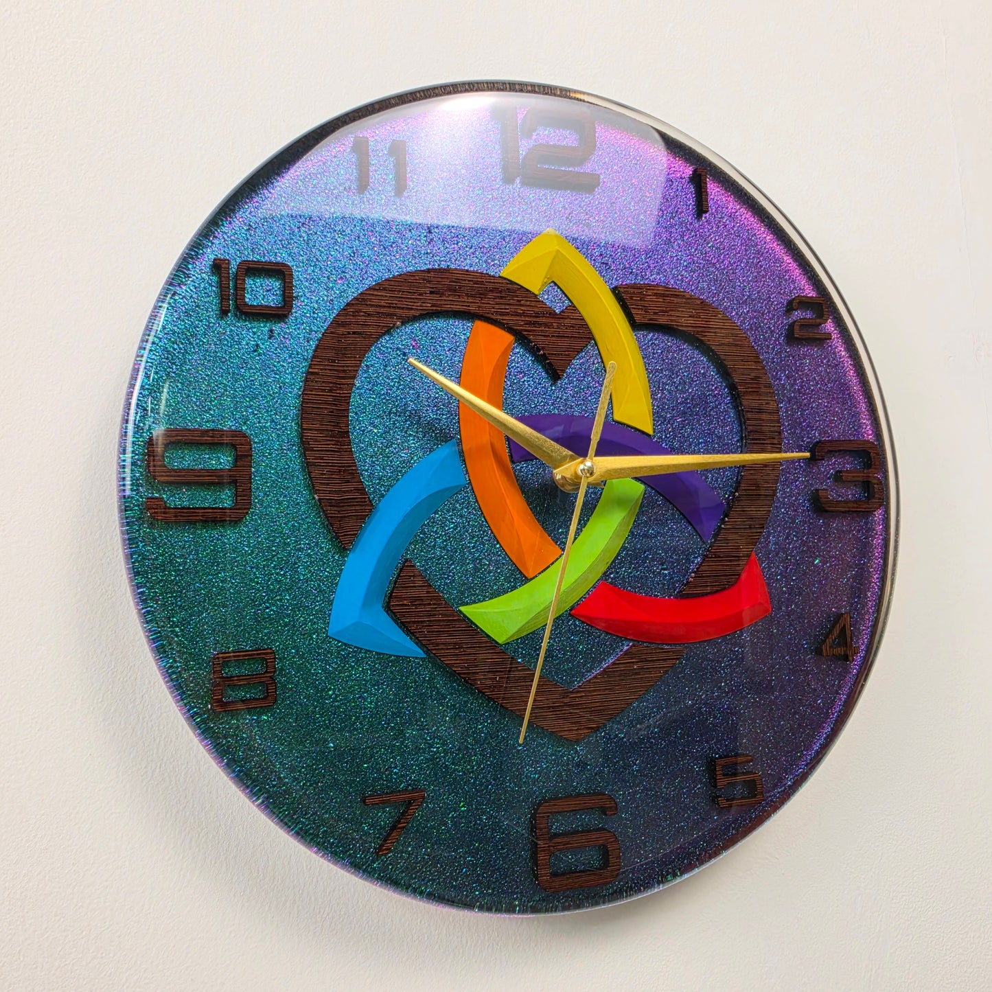Handcrafted epoxy resin wall clock featuring a wenge wood Triquetra symbol, rainbow heart, and chameleon background from the Timeless Symbols V2 collection.