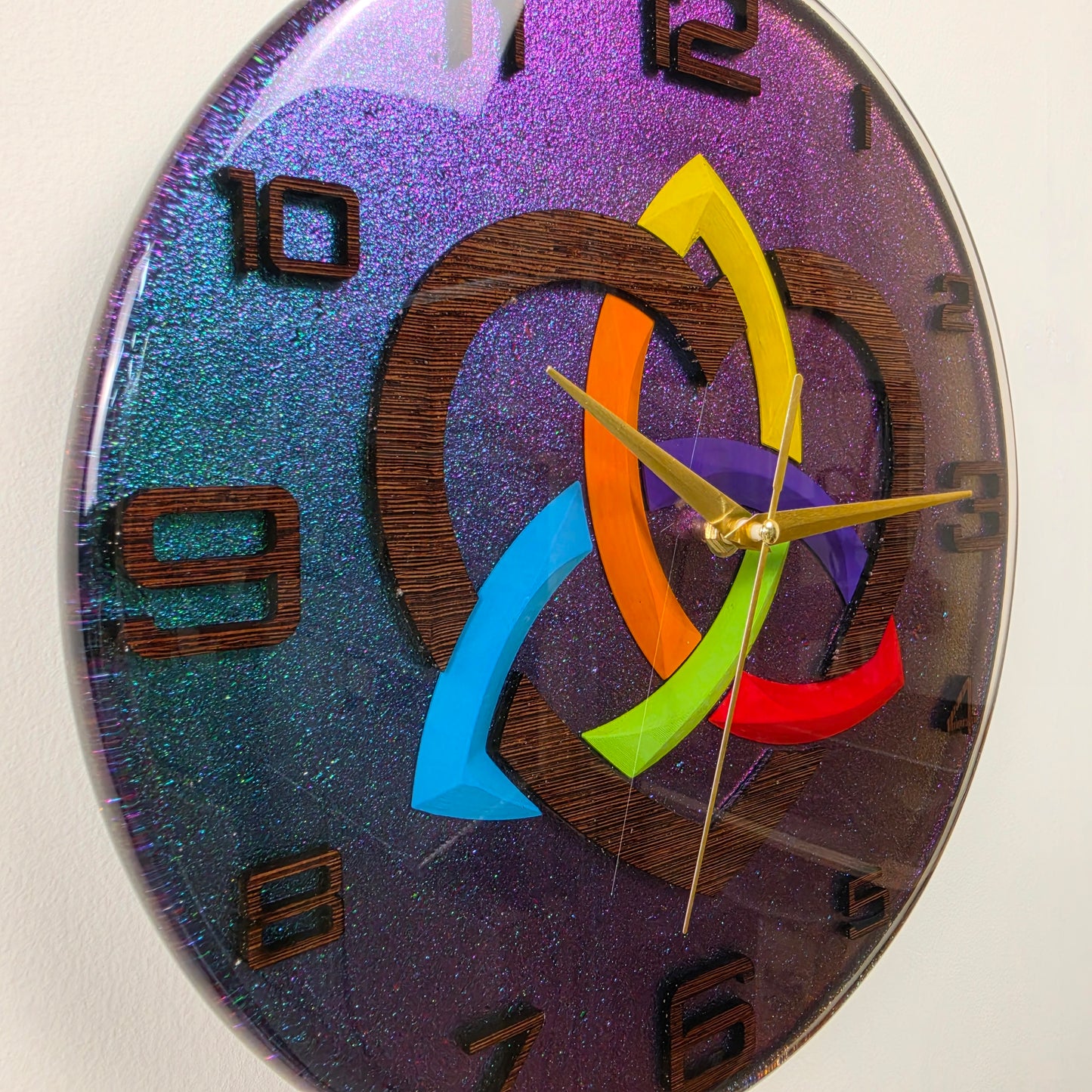 Modern resin wall clock with a handcrafted wenge wood Triquetra V2, rainbow-colored heart, wooden numbers, and silent quartz movement.
