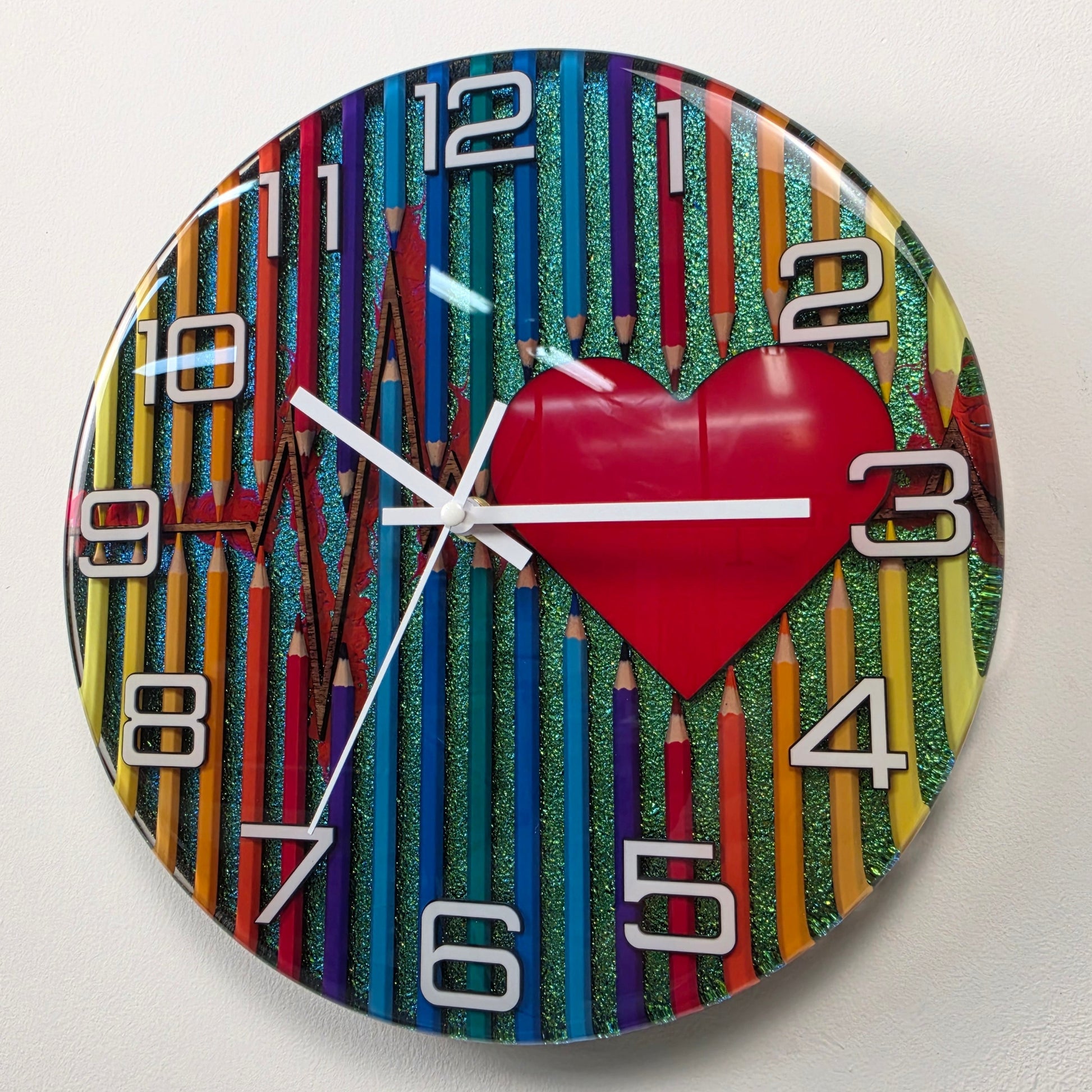 Unique 30 cm epoxy resin wall clock with colorful pencil composition, heart motif, silent quartz movement, and shimmering chameleon finish. V2