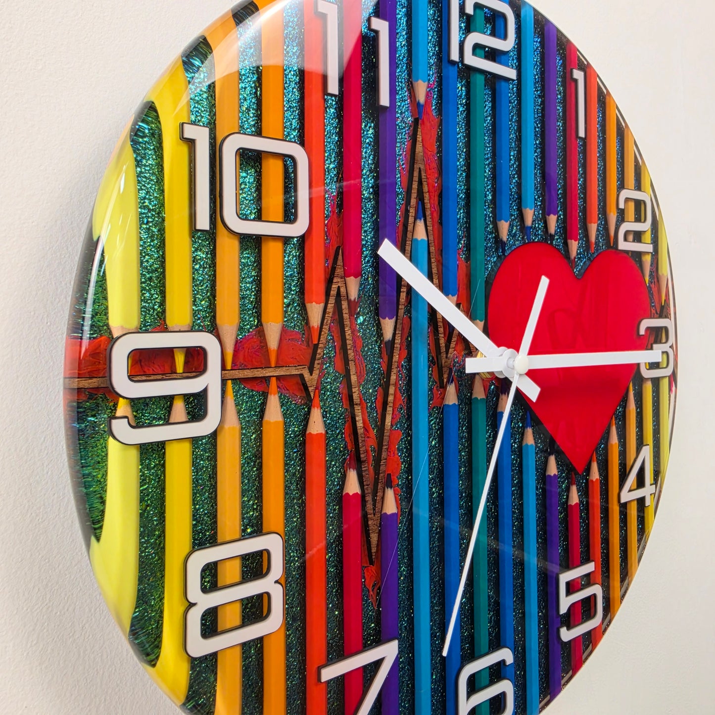 Modern artistic wall clock made with real colored pencils embedded in resin, white acrylic numbers, and a heartbeat design symbolizing imagination and creativity. V2