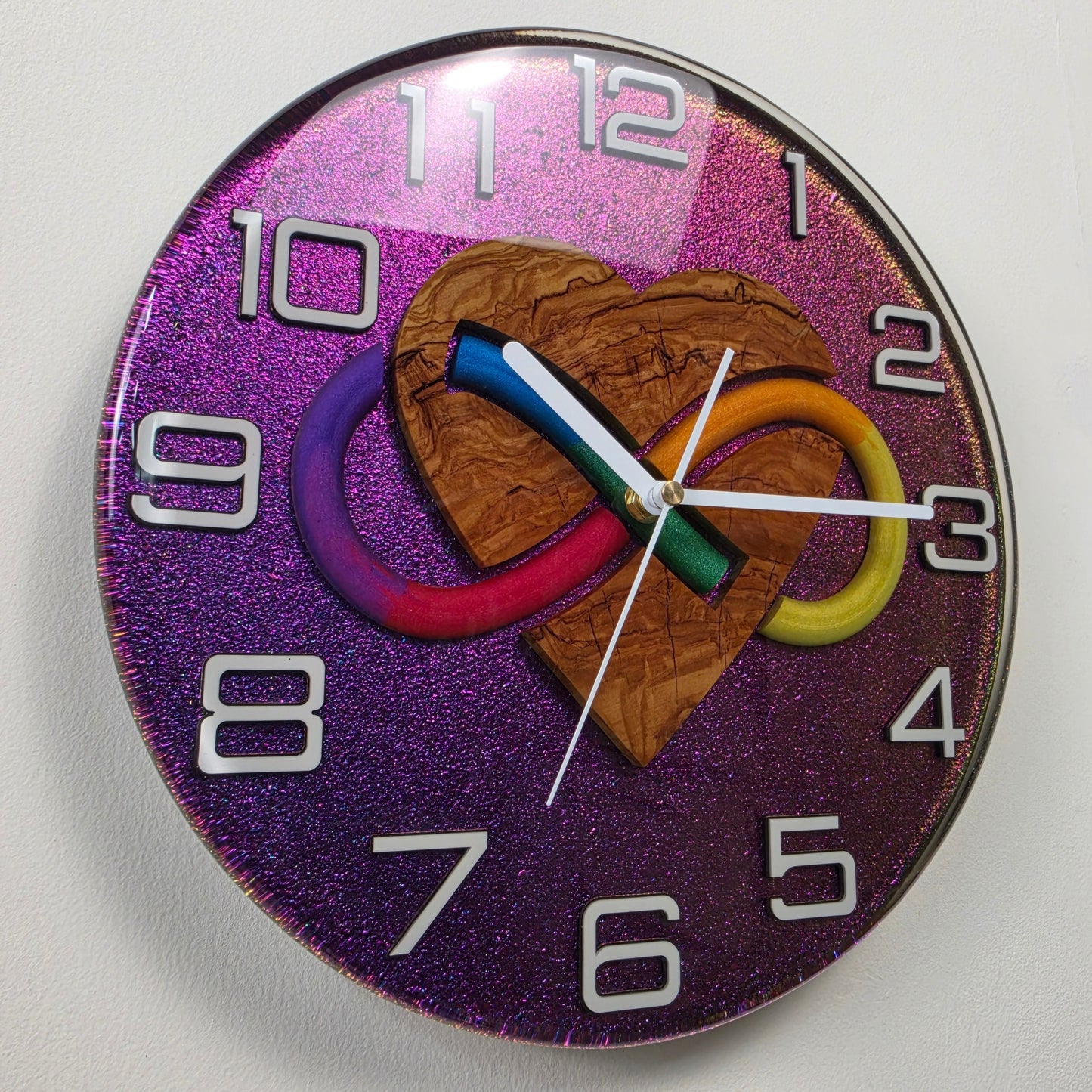 Handmade resin wall clock with an olive wood heart, colorful infinity symbol and shimmering chameleon background.