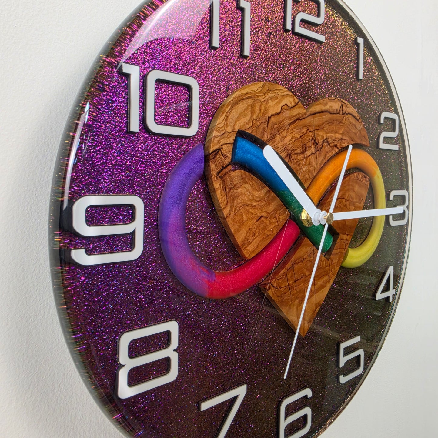 Timeless Symbols Bound Forever wall clock featuring a natural olive wood heart and multicolor infinity design in clear resin.