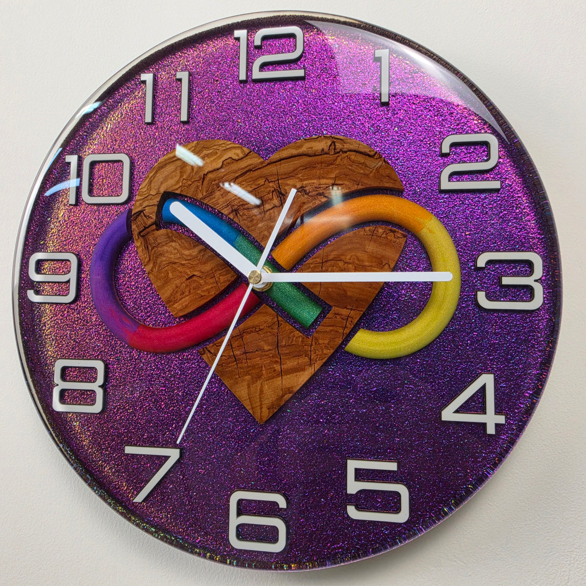 Close-up of a unique 30 cm handmade wall clock with olive wood heart, infinity symbol and color-shifting chameleon resin.
