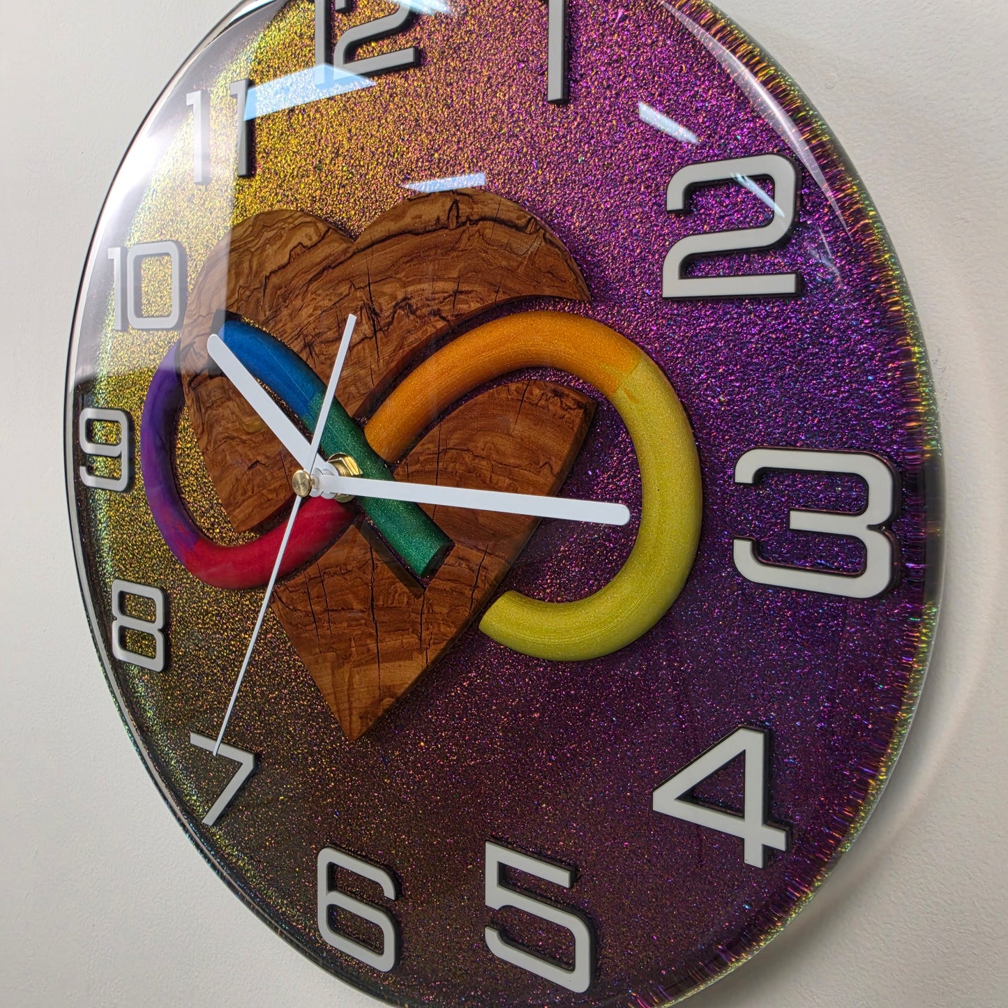 Modern artistic wall clock with a handcrafted olive wood heart, vibrant infinity symbol and white Plexiglas numbers.