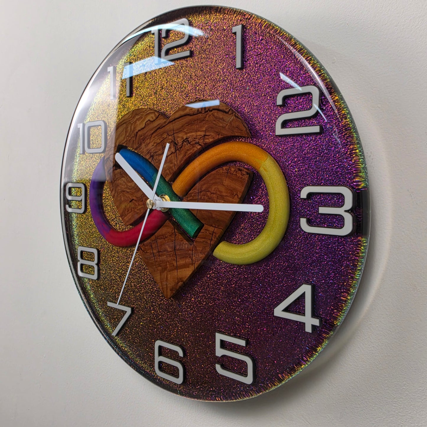 Handmade functional art clock with an olive wood heart intertwined with a rainbow infinity symbol beneath transparent resin.