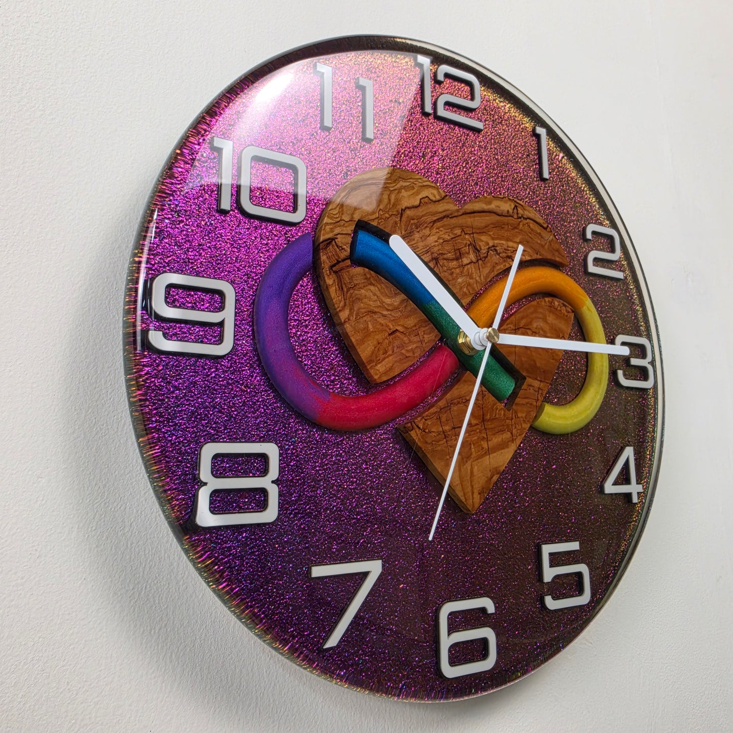 Decorative 30 cm wall clock with natural olive wood, infinity heart motif, white numbers and shimmering resin background.