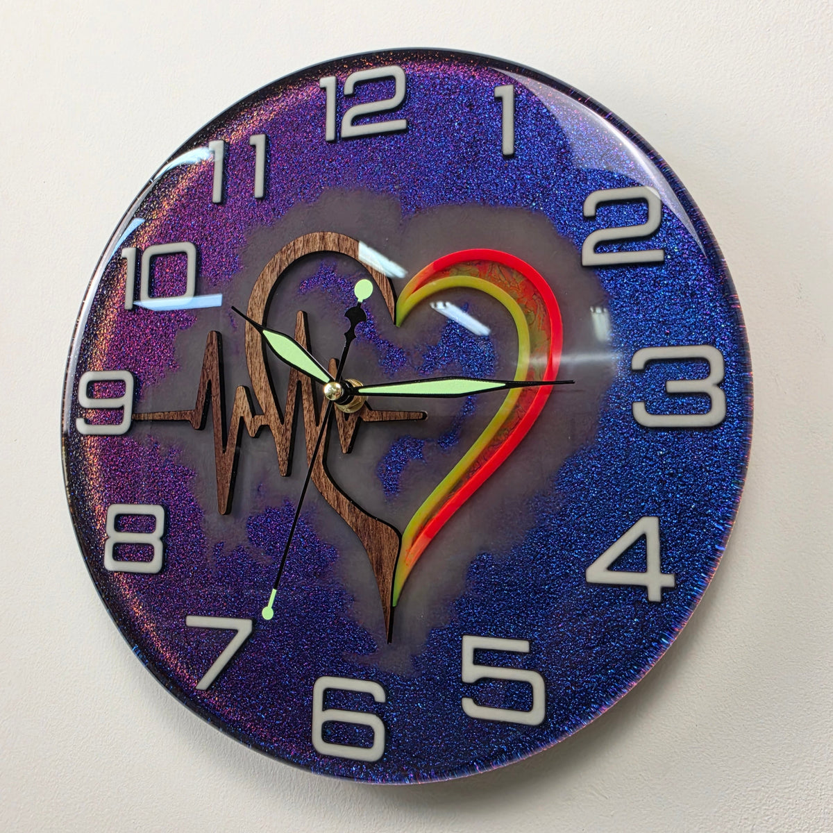Glow-in-the-dark wall clock with illuminated numerals, fluorescent heart background and glowing clock hands.