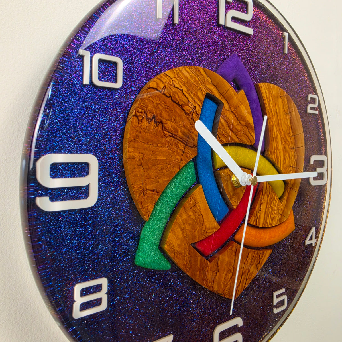 Handmade olive wood wall clock featuring an interwoven heart design with colorful resin elements.