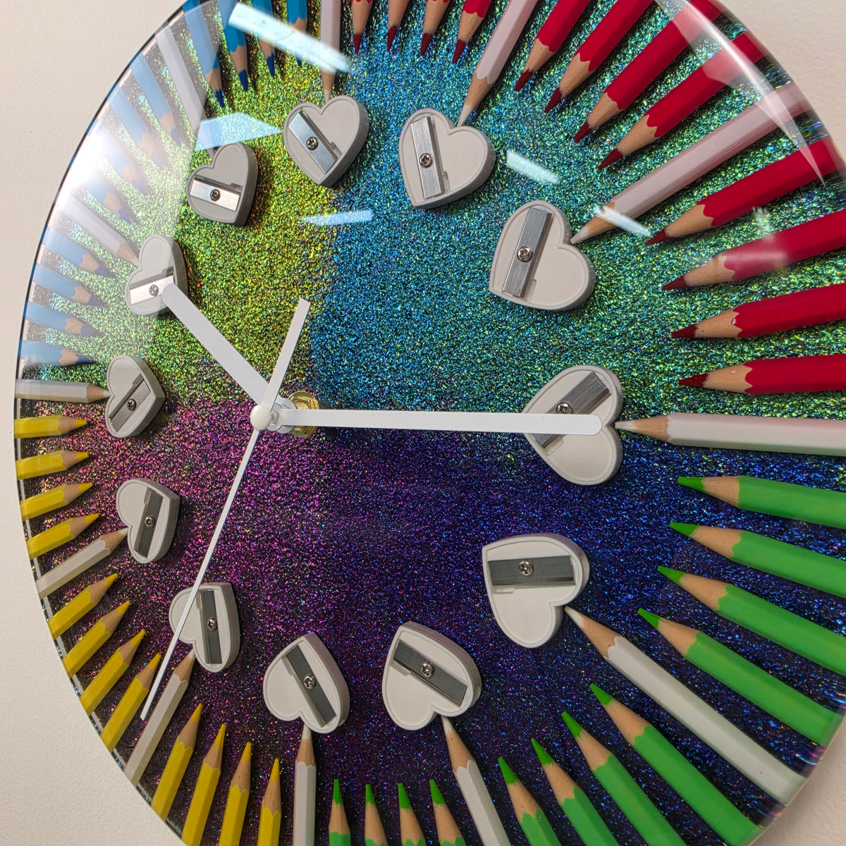 Modern handmade wall clock combining colorful pencils, shimmering chameleon pigment, clear resin and heart-shaped sharpeners.