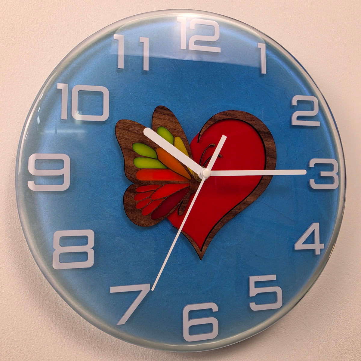 Handmade Wings of Love resin wall clock with a red heart, colorful butterfly wing and blue background.