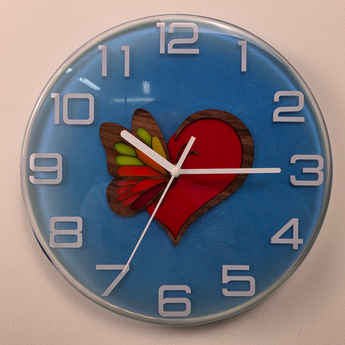 Side view of a handmade epoxy resin wall clock showing its glossy transparent finish and three-dimensional heart design.