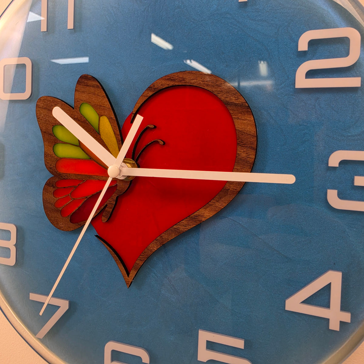 Front view of Wings of Love artistic wall clock with white numerals and a glossy blue resin dial.