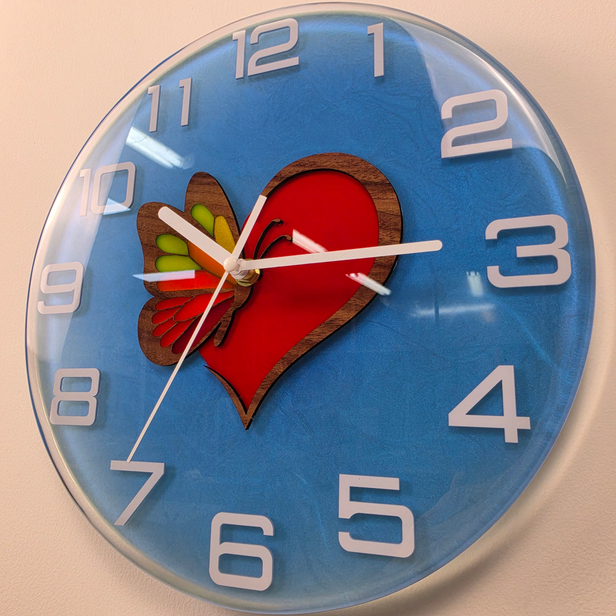 Decorative blue wall clock with a red heart, natural wood details and white clock hands, handmade in Italy.