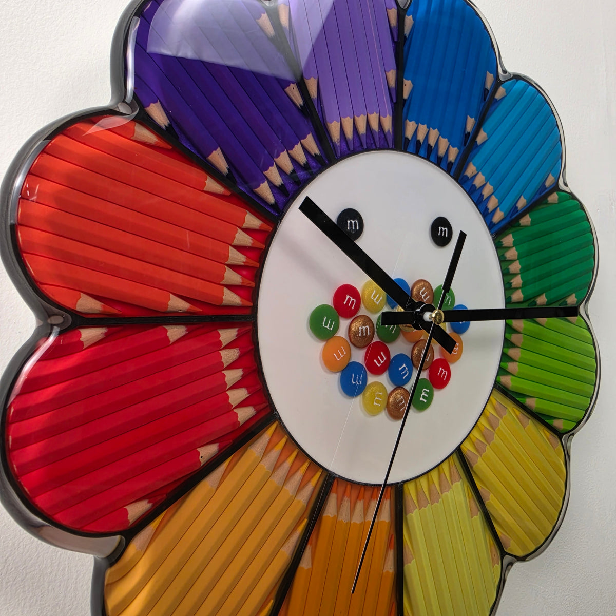 Unique flower-shaped wall clock with black hands, colorful pencil petals and a glossy epoxy resin surface.