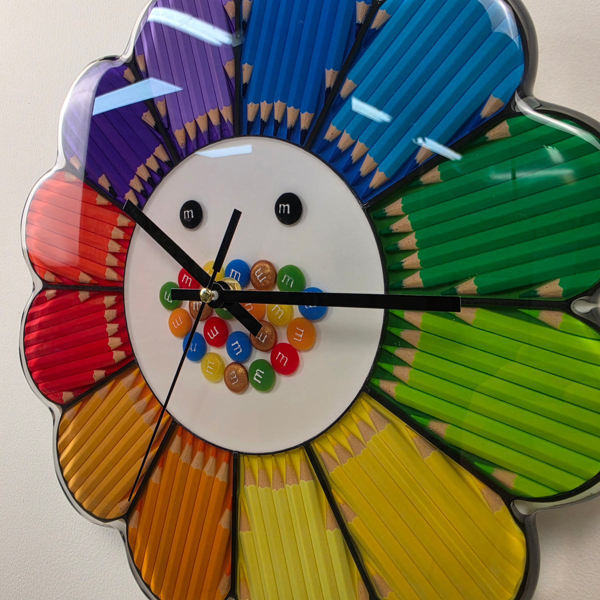 Studio Colors Rainbow Bloom artistic wall clock featuring rainbow-colored pencil petals and a white center.