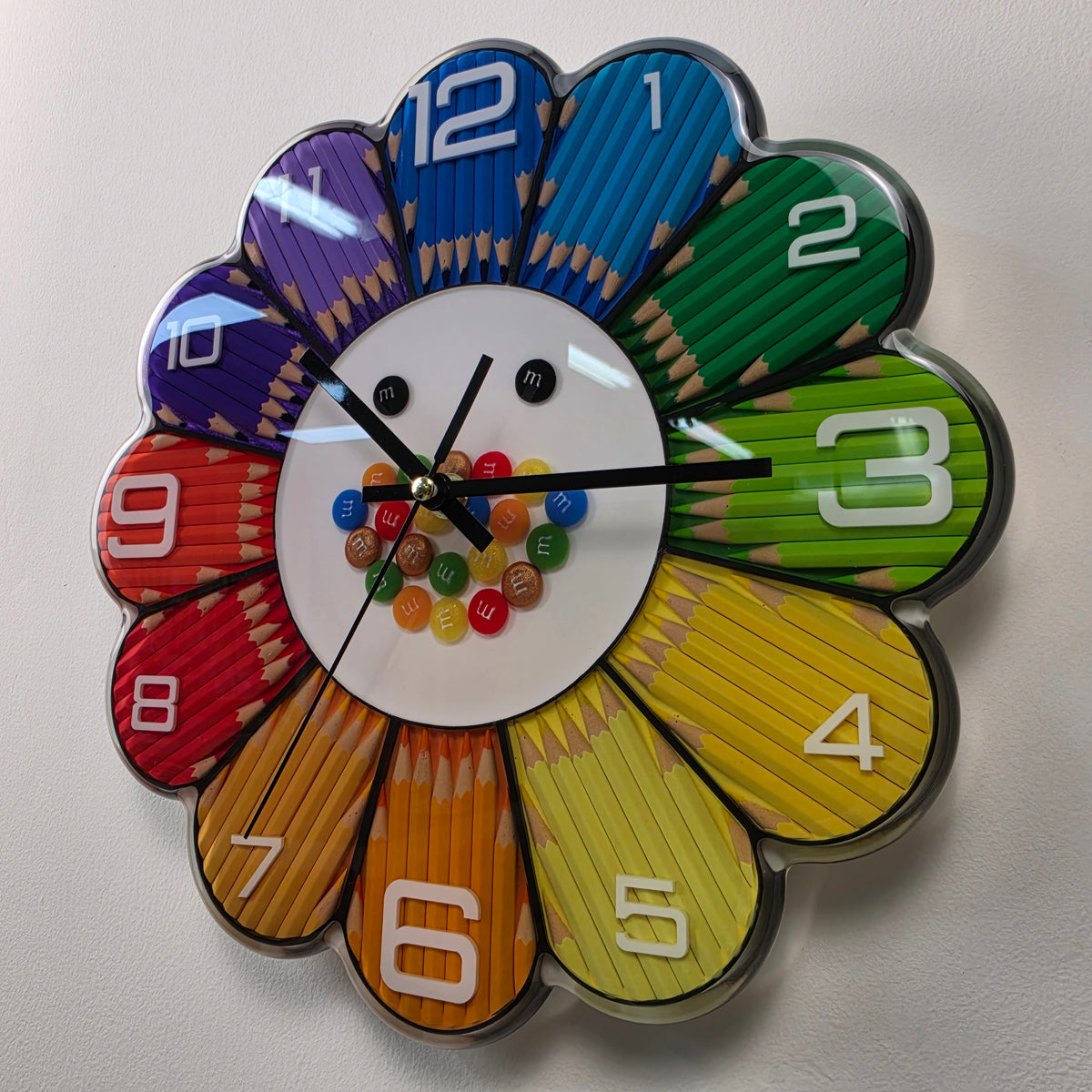 Angled view of Rainbow Bloom Numbers showing its glossy transparent resin finish, black clock hands and white numbers.