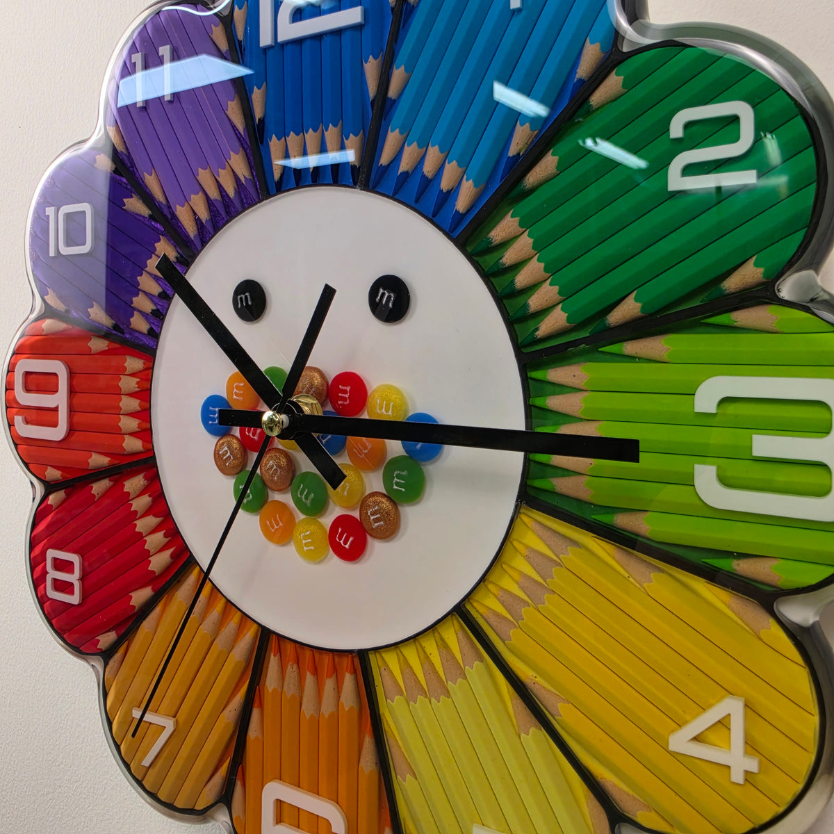 Studio Colors Rainbow Bloom Numbers artistic wall clock featuring rainbow-colored pencil petals and raised white hour numbers.