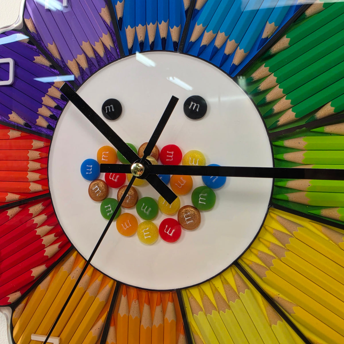 Colorful flower-shaped wall clock featuring raised white numbers from 1 to 12 on rainbow-colored pencil petals.