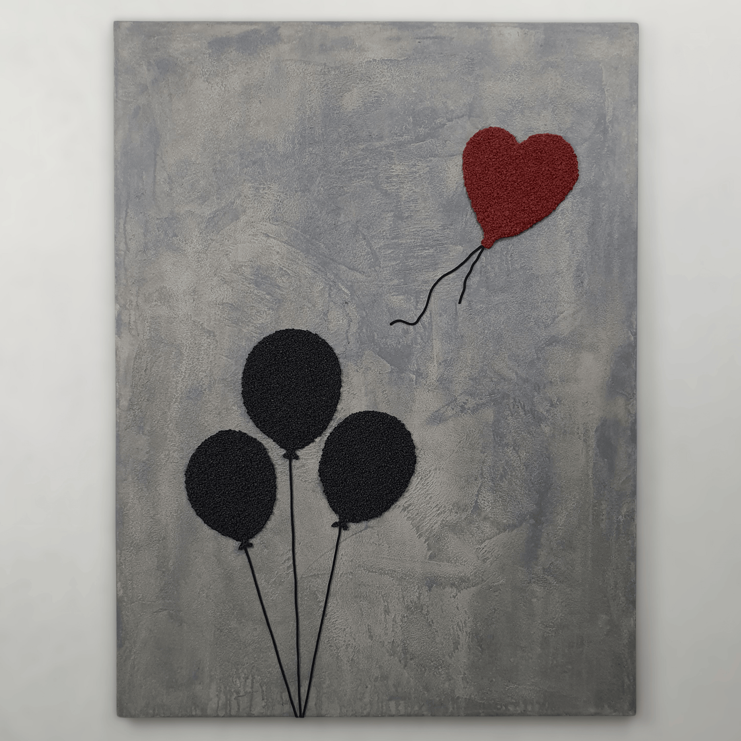 Ero con Loro conceptual artwork – three black balloons and one red heart balloon on grey textured background, front view