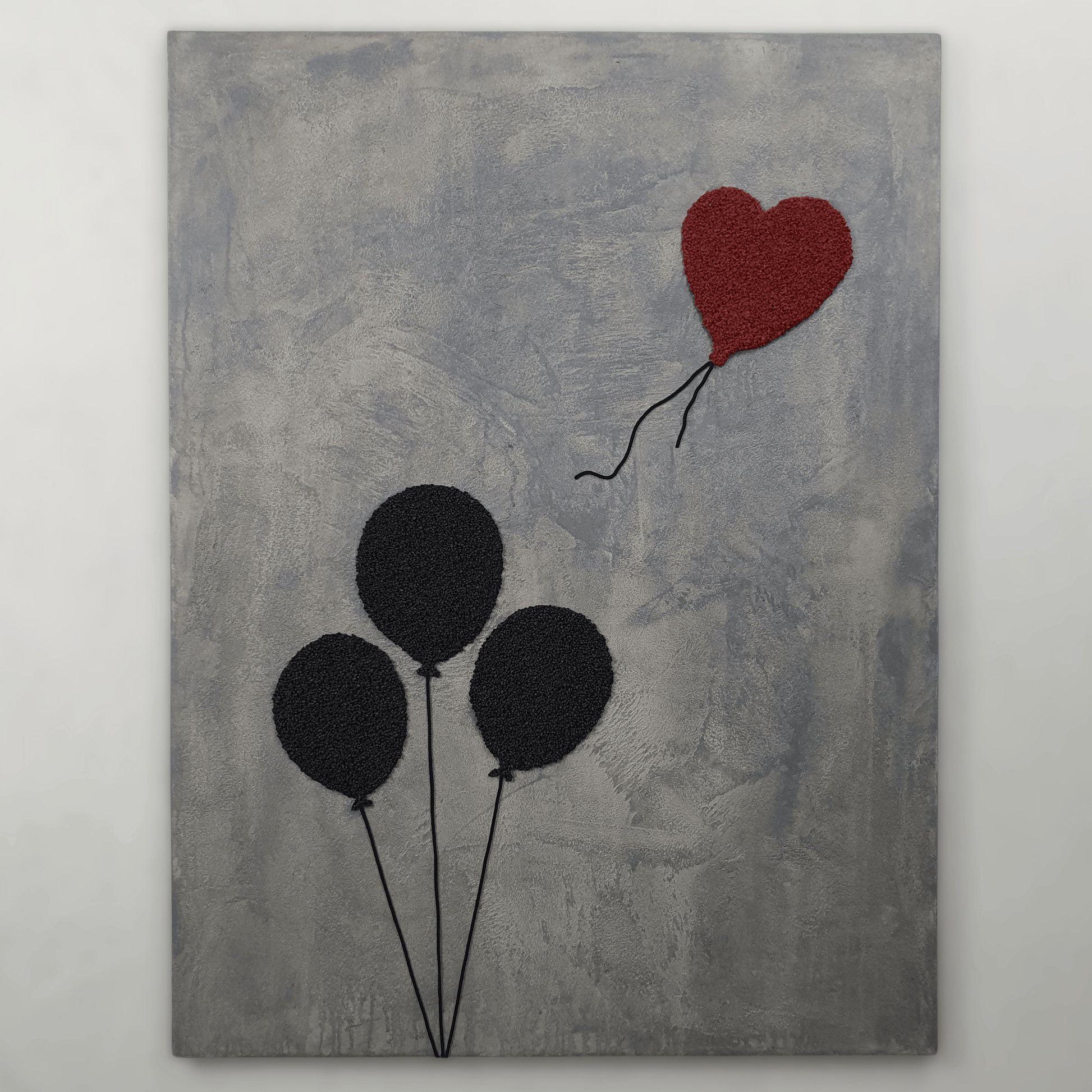 Ero con Loro conceptual artwork – three black balloons and one red heart balloon on grey textured background, front view