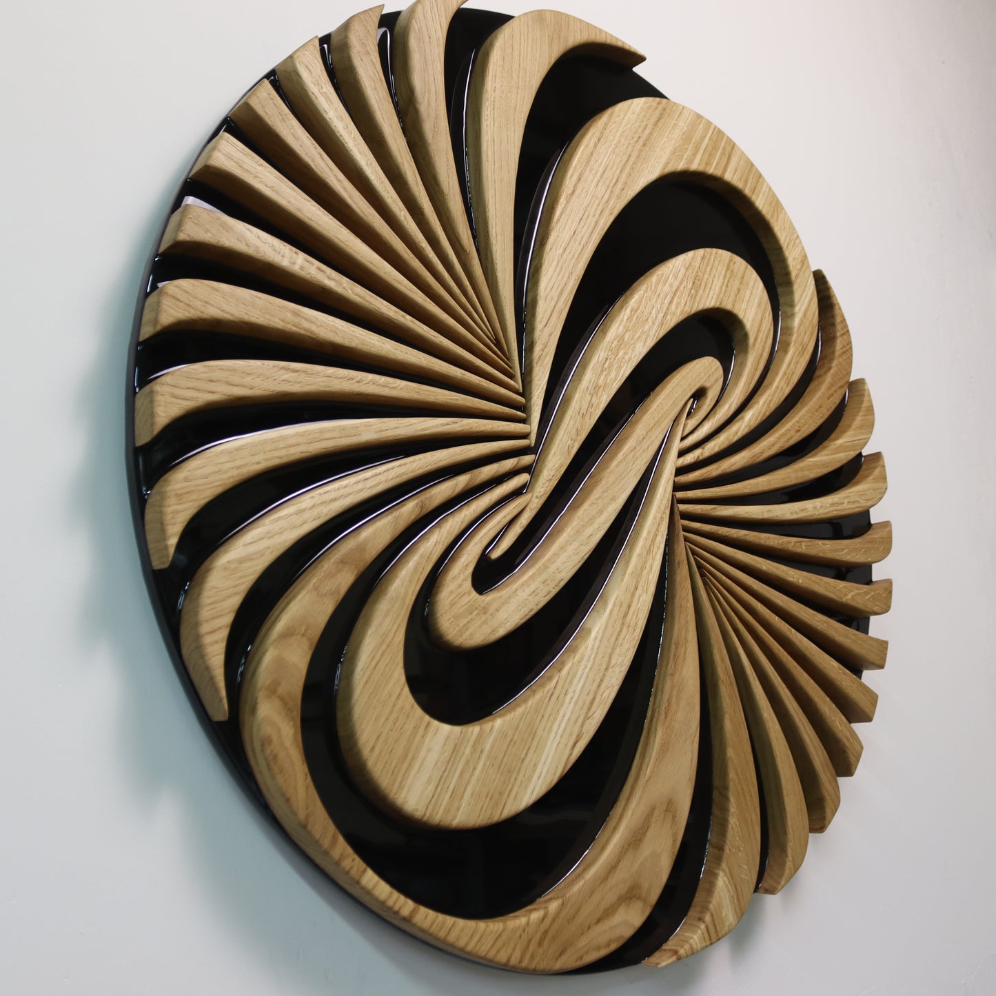 Front view of round wooden wall sculpture Vortice, geometric swirl pattern in oak and resin
