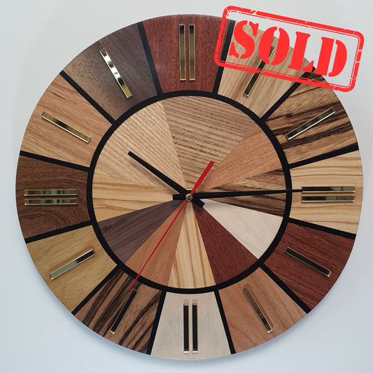 Frontal view of the Ten Woods Circle wall clock made from 10 types of wood with golden plexiglass markers